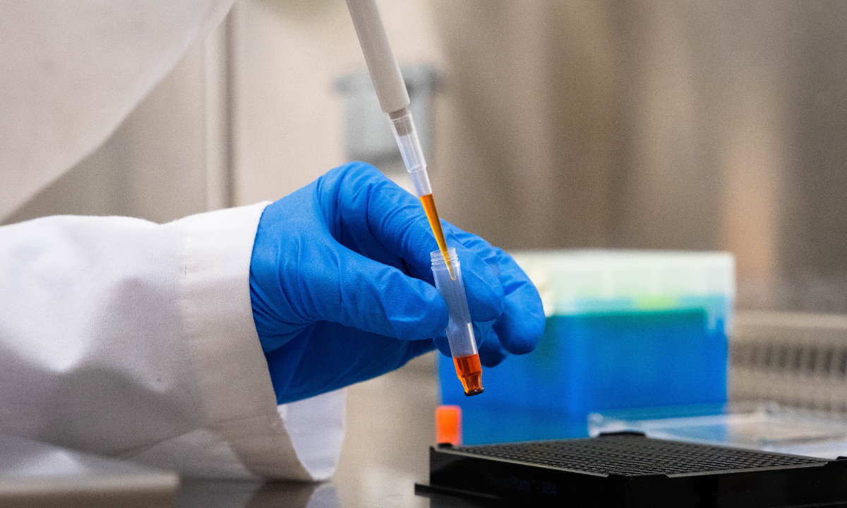 Gloved hand handling a dye-filled microtube in a lab, representing careful reagent preparation at Saguaro Biosciences